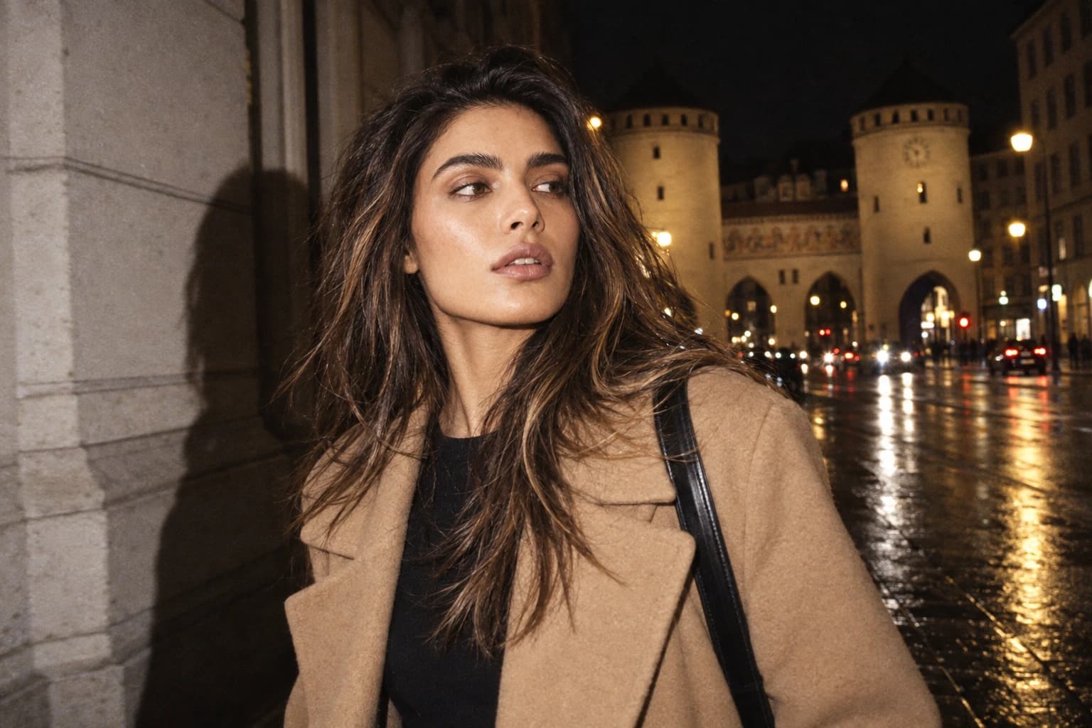 Young woman in a camel-hair coat walking at night across a rain-wet Munich street, the towers of the Isartor in the background, flash — Ästhetik am Isartor practice in Munich