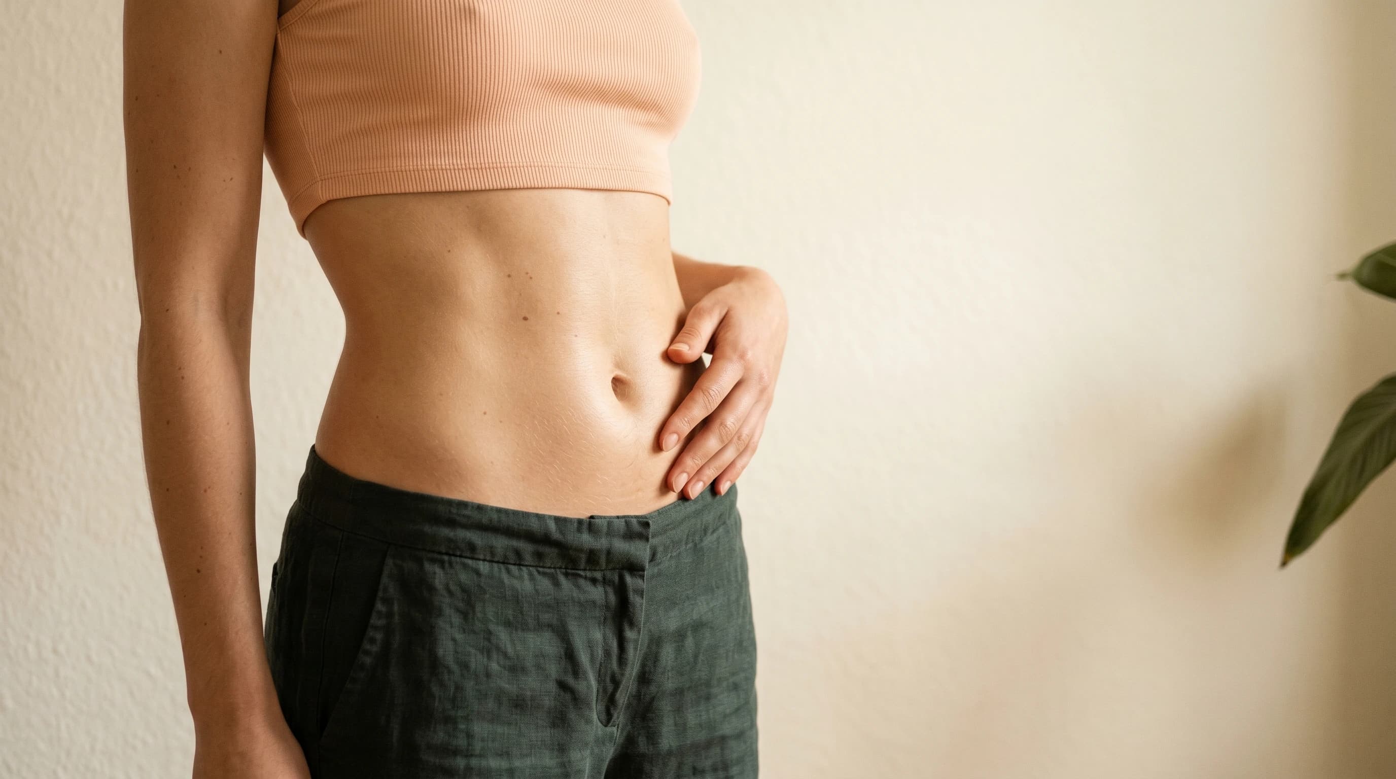 Editorial Mittelbauch in peach Strick und charcoal-grünen Leinenhosen — Körperbild Praxis Ästhetik am Isartor München