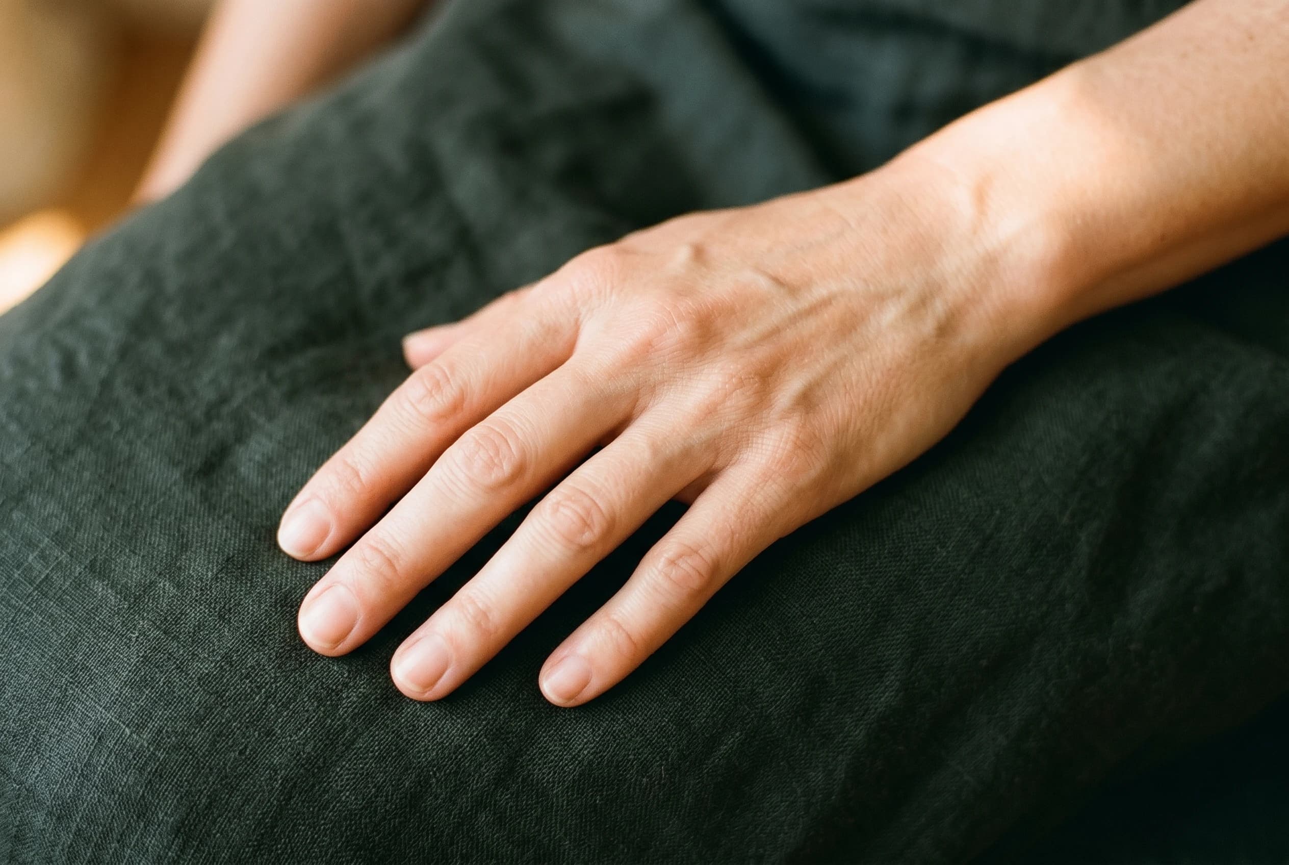 Ästhetisch fotografierte, gepflegte Hand auf charcoal-grünem Leinen in weichem Licht — natürliches, wiederhergestelltes Volumen