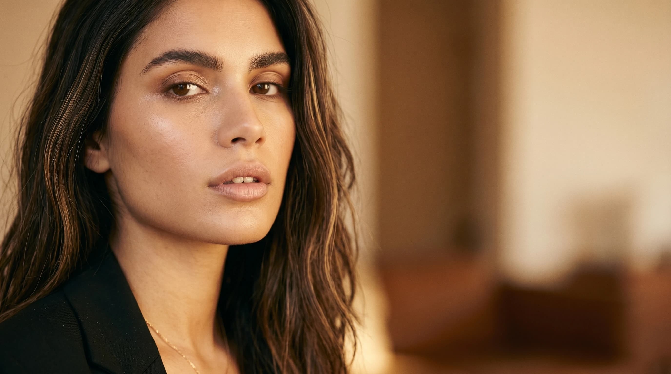 Editorial beauty portrait of a young woman with a calm lip and chin area in an elegant black blazer, warm window light — lip fillers, Ästhetik am Isartor practice, Munich