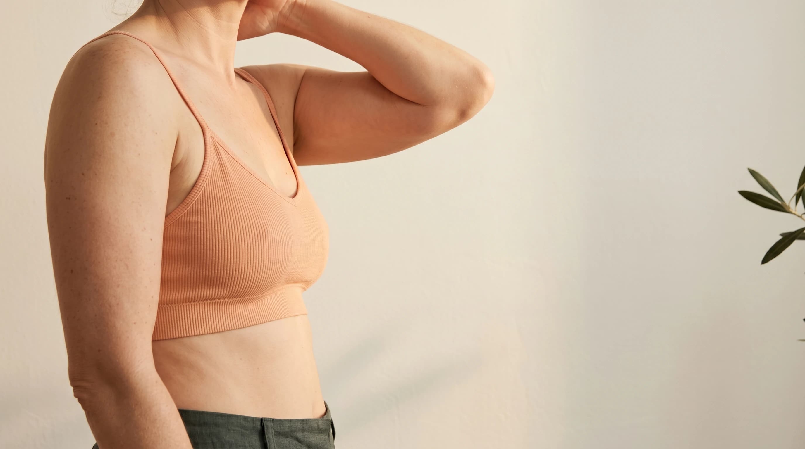Editorial upper body in peach knitwear with a raised arm — the natural contour of the inner upper arm. Ästhetik am Isartor practice, Munich