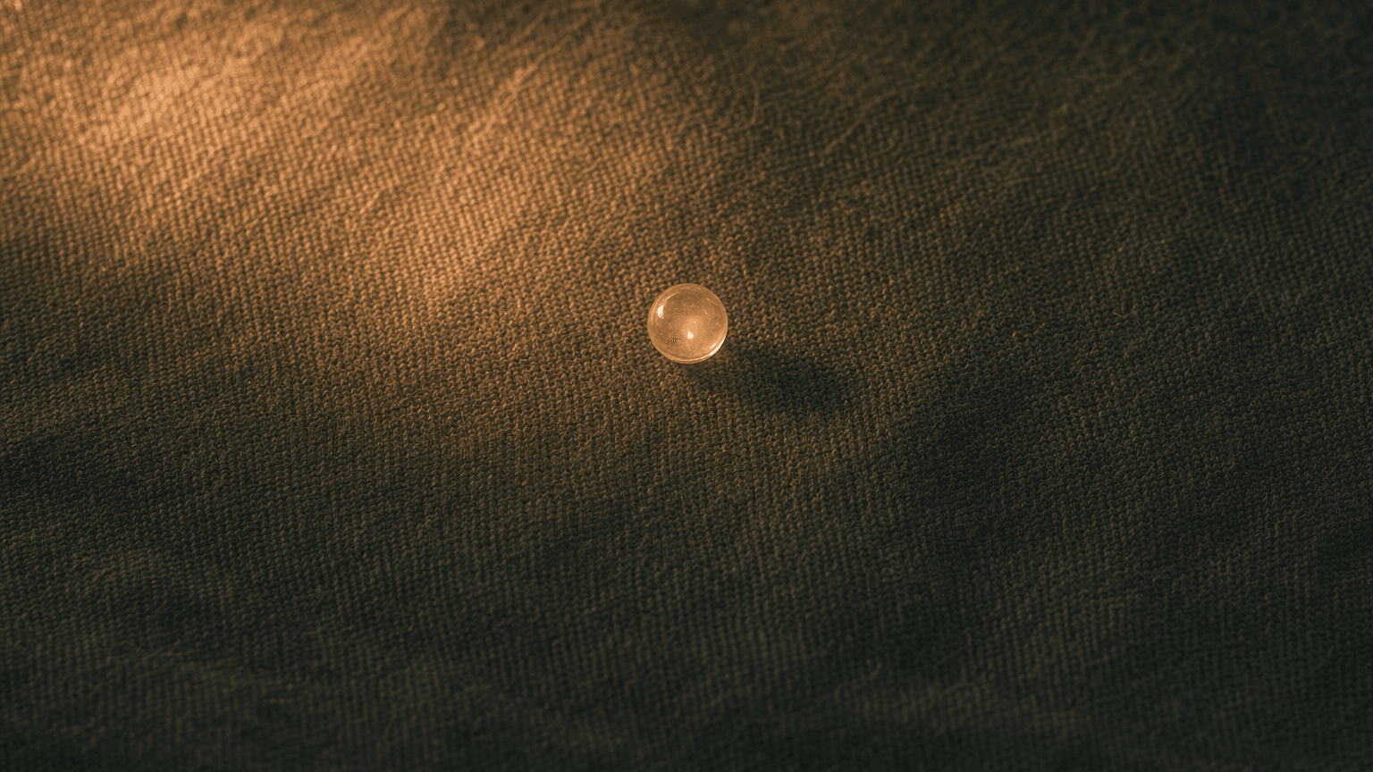 Soft peach plasma-glow auf charcoal-grünem Leinen mit kleinem peach Glas-Marmor in der Mitte — atmosphärische Textur des kühlen Plasmas