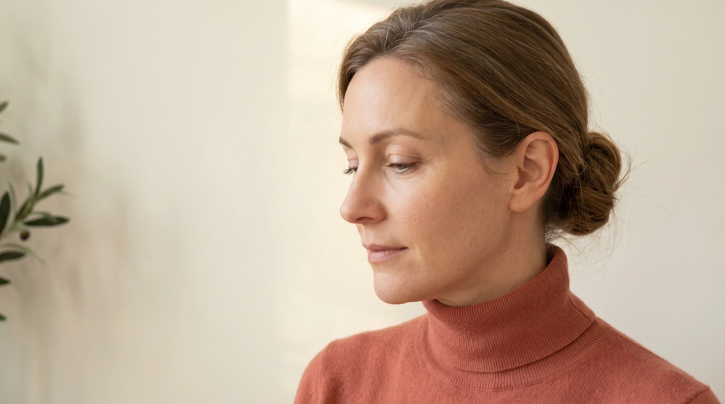 Editorial Drei-Viertel-Profil mit gesenktem Blick, dusty-coral Cashmere-Rollkragen — Praxis Ästhetik am Isartor München
